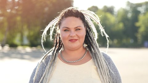 Concept of diverse beauty and lifestyle. Portrait of happy smiling woman with dreads posing for camera at beautiful sunny summer day. Pretty fat or stout girl showing body positive attitude to herself