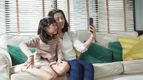 Asian family making a video call and waving at the caller with daughter in living room at home.