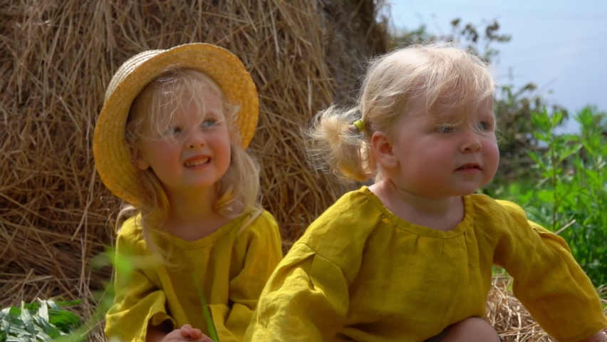 Cute little blond girls are stroking the little duckling on the background of haystack