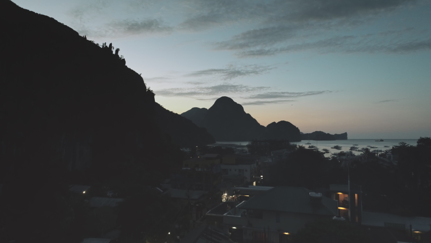 Slow motion night port town with traffic road at sea bay. Aerial pier cityscape at mountain silhouette of ocean gulf. Highland islands of El Nido, Philippines archipelago. Cinematic drone shot