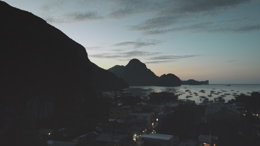 Slow motion night port town with traffic road at sea bay. Aerial pier cityscape at mountain silhouette of ocean gulf. Highland islands of El Nido, Philippines archipelago. Cinematic drone shot Royalty-Free Stock Footage #1061602456