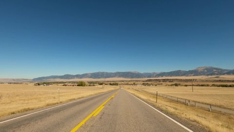 Long straight Highway 287 toward Ennis Montana passing dry amber fields with the Madison range in the background-Drive Plate-POV