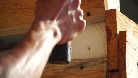 Hands of the person with electric tool unscrew the self-tapping screw from a wooden board. Screwing the screw in a wooden board. 4k Closeup Video.