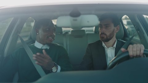 Multi-race couple of business partners commuting to corporate office driving car together having interesting conversation during roadtrip. Businessmen. Friendship. Successful.