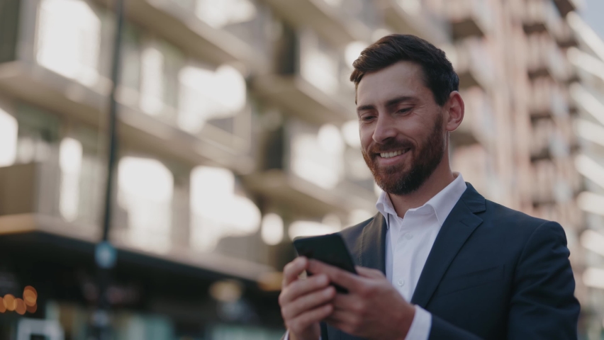 Successful happy caucasian young adult bearded businessman commuting to work using smartphone chatting messages smiling walking the street outdoor. Business people. Royalty-Free Stock Footage #1061608936