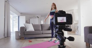 Caucasian woman spending time at home, in living room, exercising, stretching and recording it with a camera in slow motion. Social distancing during Covid 19 Coronavirus quarantine lockdown.
