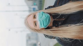 Concerned woman in medical coronavirus mask walking on the street. City buildings and road on the background. Coronavirus pandemic concept. Video with Vertical Screen Orientation 9:16
