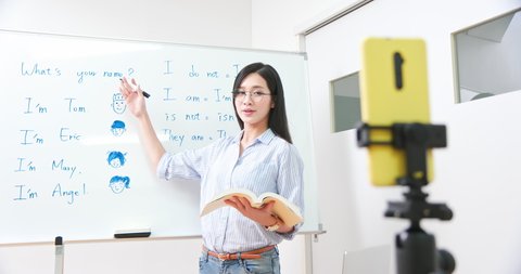asian female teacher teach english for children online through mobile phone in classroom