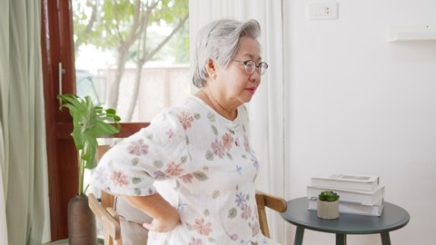 Old Asian senior woman feel pain, ache, hurt at back while standing and sitting at home, back pain concept