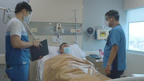 Elderly Man With Illness Lying On The Hospital Bed And Being Checked By A Doctor And A Nurse With Face Mask
