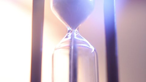 Macro footage of sand falling through vintage wooden hourglass. Extreme close up of lens flare in old fashioned sand timer.