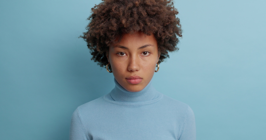 Uncertain clueless woman with Afro hair hesitates about something says no and feels puzzled dressed in casual turtleneck isolated over blue background. Indecisive questioned young female poses indoor | Shutterstock HD Video #1061620735