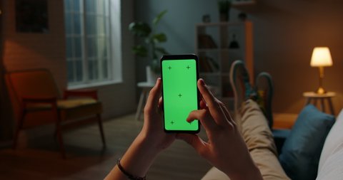 Man lying on couch using smartphone with chroma key green screen at night, scrdoing various gestures like swiping and scrolling - internet, communications concept close up 4k template