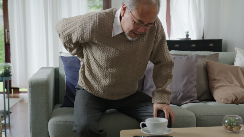 Asian elderly senior male grandpa sitting at sofa couch at home living room on quarantine in concept healthcare, chronic health issue or low back pain in retired older people. | Shutterstock HD Video #1061624137