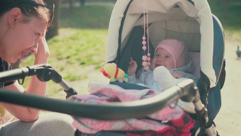 The Little Baby Lies in the Stroller and Smiles at the Mom Who Plays with the Baby. Childhood Positive, Family Love. Warm and Sunny Day.