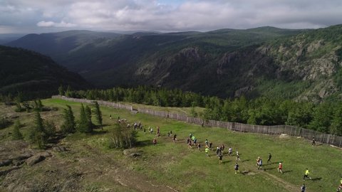 Aerial 4K shot. A group of people runs in a chain down the hill of the mountain. Great view of the mountain peaks.