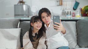 Asian family little kid girl and mother talking in video conference by smartphone together in living room at home with happiness and smile. Happy activity technology lifestyle mobile phone use concept