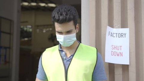 Young Indian factory warehouse worker wearing a protective face mask and safety helmet with factory shutdown notice sign - HD Slow Motion Footage