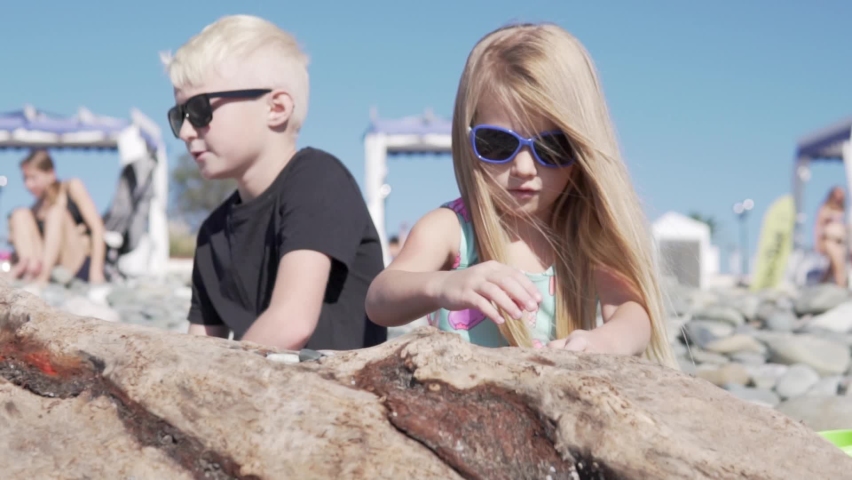A cute brother and sister play with stones on a pebble beach in Sochi.