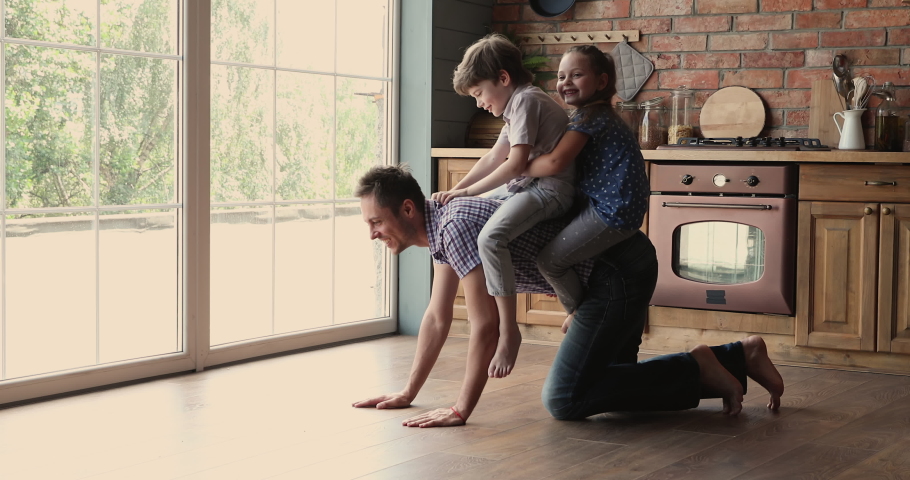 Little children sitting on daddy back riding having fun play together in kitchen. Dad crawling on warm wooden floor enjoy leisure funny time with pretty son and daughter, leisure, modern house concept Royalty-Free Stock Footage #1061639674