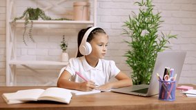 little child girl using laptop for doing school tasks at home and writing notes. online lesson at home