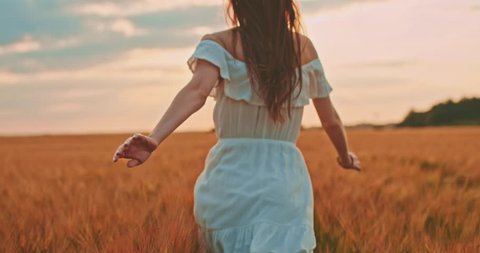 Beautiful girl running on sunlit wheat field. Slow motion 120 fps. Sun lens flare. Freedom concept. Happy woman having fun outdoors in a wheat field on sunset or sunrise. Slow motion. Harvest. 