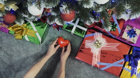 Christmas gifts. Female hands lay heart near a beautiful Christmas tree, a symbol of love, family happiness. Colorful decorated New Year tree view from the top