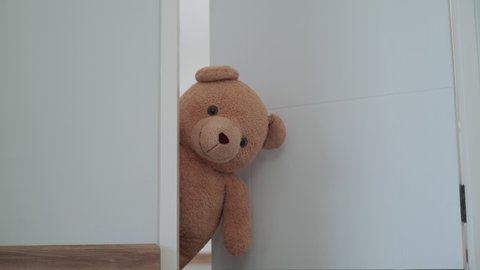 A brown teddy bear hidden inside the room near the door.A brown teddy bear poked his face from behind the wall.
The brown teddy bear poke a face next to the door, the face of teddy bear look smiling.