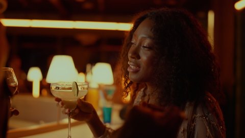 Closeup african american woman resting in night club party. Beautiful afro girl holding cocktail in bar. Portrait of gorgeous woman dancing in restaurant with unrecognizable man at evening