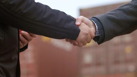Businessmen Engineers shake hands as they load a container from a container yard onto a cargo ship for global import and export, supporting the concept of logistics. Close-up.