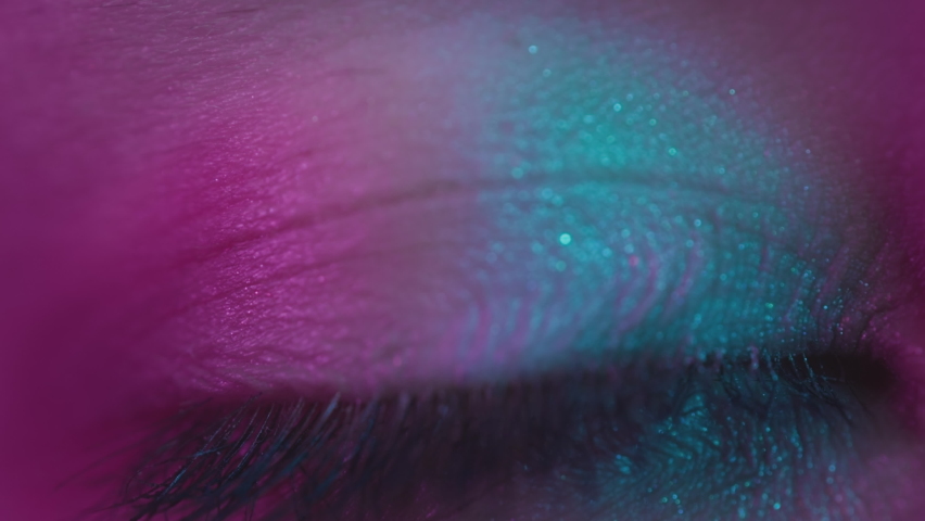 Close up shot of eye opening with pink iris. Healthy eyesight concept. Female pink eye in neon light. Young sexy girl in a nightclub. Macro look of the human eye. Pink-blue-green color, euphoria.