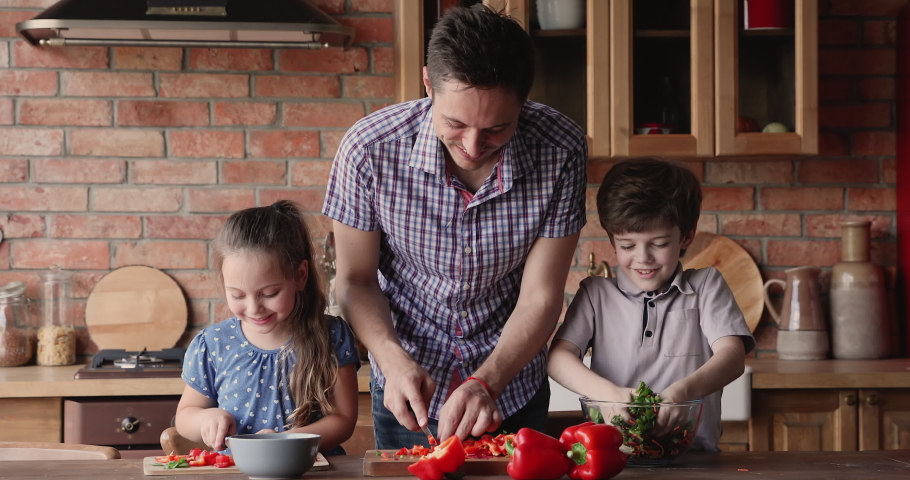 Father and little children prepare together salad in home kitchen slicing vegetables preparing healthy organic fresh dinner. Kids development and upbringing, hobby activity and food delivery concept | Shutterstock HD Video #1061658331