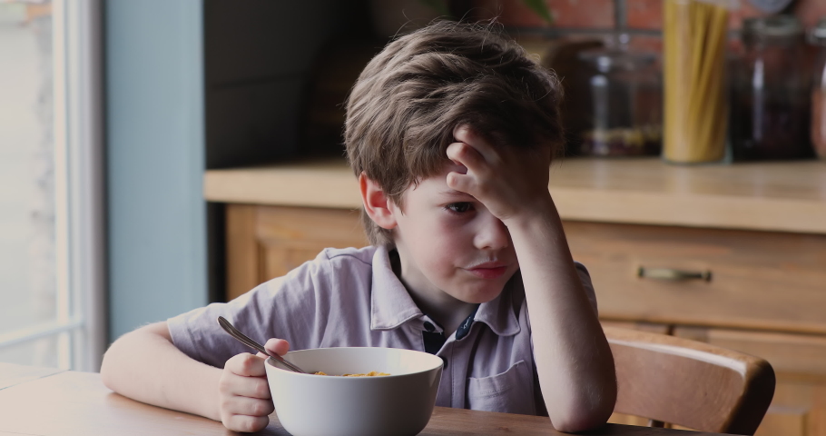 Little  boy sitting at dining table in kitchen in front of bowl with milk and corn flakes, kid feels sluggish without appetite lack of energy in the morning. Get up early, not tasty breakfast concept Royalty-Free Stock Footage #1061658337