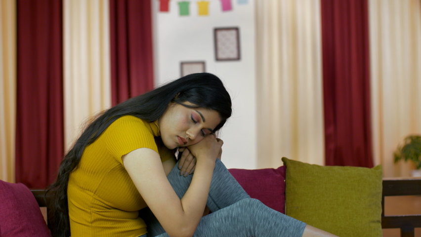 A depressed and confused woman sitting alone on a sofa in the living room . Medium shot of an upset Indian female in her early twenties facing problems in life - stressed urban lifestyle Royalty-Free Stock Footage #1061659978