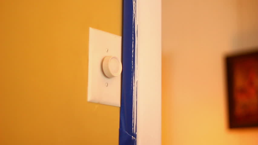 A painter removes blue painter's tape after painting trim in a house.  With