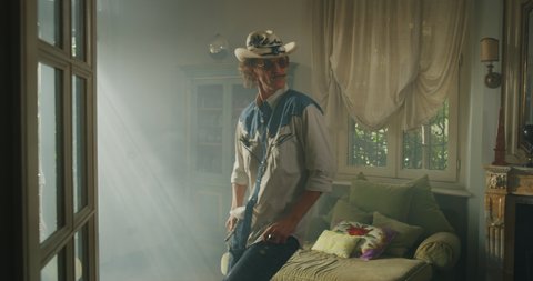 Cinematic shot of an young carefree happy man with moustache wearing cowboy hat and sunglasses is having fun to listening to the music and dancing crazy in a living room at home.