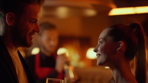 Young man drinking cognac at nightclub party. Beautiful woman having rest in bar at evening. Handsome man flirting with young woman in restaurant interior. Young couple dating at night club