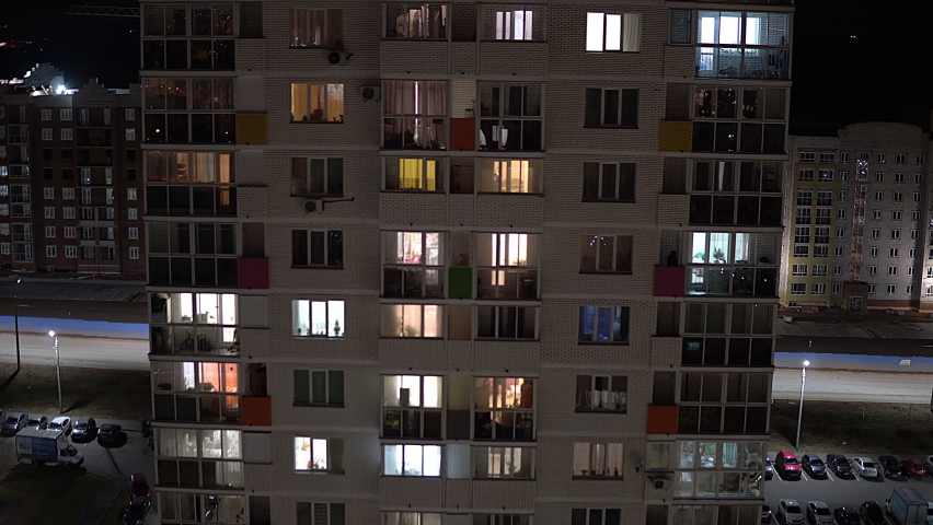 Tall multi-storey building in the evening. In the windows of apartments people are busy with their own affairs
