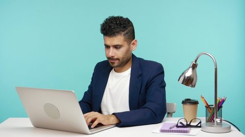Male office worker feeling pain in back working on laptop in his office, problems with spine or kidneys, sedentary lifestyle. Indoor studio shot isolated on blue background