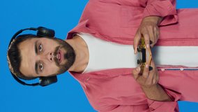 Close-up.Man playing video game on a blue background. He is surprised by what is in the game. Slow motion video.Video for the vertical story.
