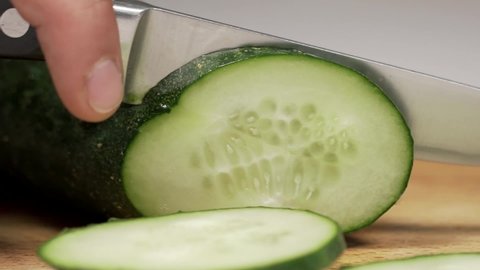 Hand Cuts Cucumber Rings CloseUp. Hands slicing fresh cucumber on a wooden cutting board. Slicing vegetables with a knife for cooking. Stock footage. 