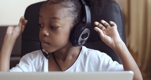 Portrait of Afro american kid girl school pupil wearing headphones studying online distant from home watching web class lesson or listening tutor by video call e-learning education, pandemic isolation