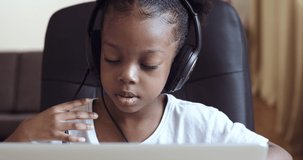 African american pupil kid studying online at laptop, mixed race afro child wearing headphones listening remote lesson sitting at home class. Little school girl learning. Children remote education.
