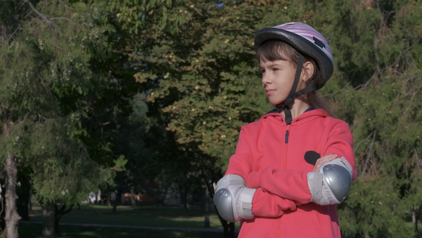 Child in rollers equipment. A teen in sporty equipment stay in the sunny park street.