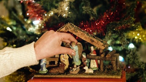 Woman puts miniature figurines of Mary in a christmas crib next to a christmas tree. Beautiful nativity scene and christmas decorations - close view