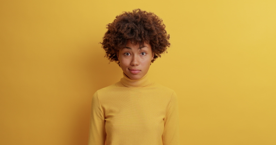 Clueless dark skinned woman throws up hands and shrugs shoulders in slow motion has doubtful expression dressed casually poses against yellow studio wall cannot help with way out makes decision Royalty-Free Stock Footage #1061690296