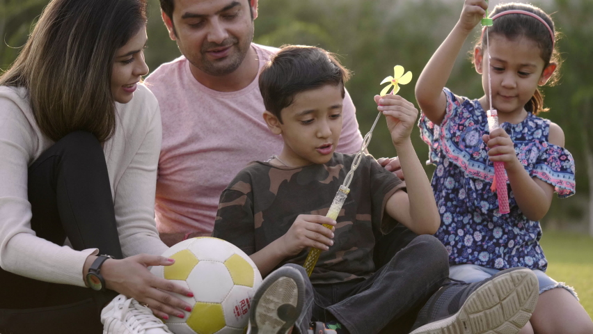 Happy family including mother, father, and two kids are blowing soap bubbles and enjoying the summer holidays in the garden or park. Smiling parents and children are spending leisure time together. Royalty-Free Stock Footage #1061690728