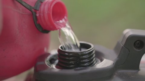 A man opens the lid of the gas tank and pours gasoline from a canister. Close-up