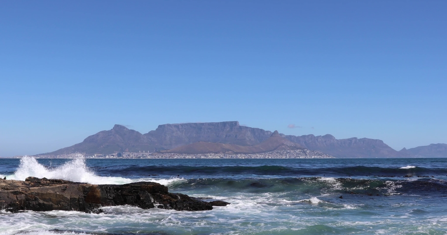 Beautiful clear day looking from Robben Island to table mountain and mother city with ocean waves crashing over rocky shore line on Robben Island 