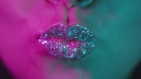 Female lips in neon ultraviolet light. Fashionable neon light, euphoria. Sexy lips kiss. Female mouth close-up. Shiny lips in a nightclub. Pink-blue-green color and new light. Metallic lipstick.